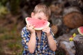 The boy holds a slice of watermelon and looks out from behind it. Positive emotions. Royalty Free Stock Photo