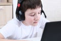 A boy homeschooler with headphones sitting at a laptop and learning, online education concept Royalty Free Stock Photo