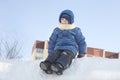 Boy In Hooded Jacket Sitting On Snow Heap