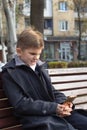 A boy with an irritated expression in a business suit sits on a bench with a smartphone.He does not like what he saw on