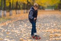 Boy in jacket standing on skateboard with one foot, going to move forward. Full length front portrait in the park covered with