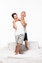 Boy jokingly stifling smiling brother while standing on bed isolated on white