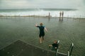 Boy jumping off jetty at the Bogey Hole in Newcastle, NSW on an overcast day with rough surf