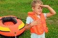 Boy keeps watch and inflatable boat on lawn Royalty Free Stock Photo