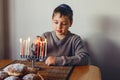 Boy in kippah lighting candles on a menorah for traditional winter Jewish Hanukkah holiday. Child celebrating Chanukah festival of Royalty Free Stock Photo