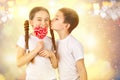 Boy kisses little girl with candy red lollipop in heart shape. Valentine`s day art portrait Royalty Free Stock Photo