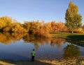 Boy by lake with fall colors in trees.