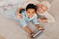 Boy laying at floor and using tablet while relaxing with his grandfather Royalty Free Stock Photo