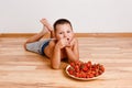 Boy lies on the floor on his stomach and eats strawberry berries