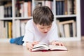 Boy lies on his stomach and reading a book in the library Royalty Free Stock Photo