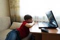 The boy lies in the living room on the couch and watches a movie on a laptop.