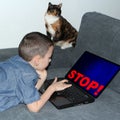 Boy lies on a sofa in front of an open laptop, dark technological background on the display and large STOP inscription in red