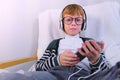 Boy is listening music in headphones in smartphone and singing a song sitting in armchair at home. Royalty Free Stock Photo