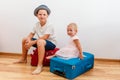 Boy and little girl sit on large suitcases in the room