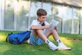 Boy looks concentrated while doing homework with a notebook sitting on the grass outdoors. Royalty Free Stock Photo