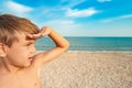 The boy looks into the distance, covering his face with his hand from the sun on the beach, by the sea Royalty Free Stock Photo