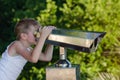 Boy looks through telescope at city sights. On background of summer Park