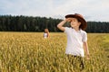 A boy looks up to the sky at the wheat field in a cowboy hat and a girl on a distant background Royalty Free Stock Photo