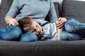 The boy is lying on the couch with an abdominal pain near his mother. The concept of custody, parental care, stomach problems,