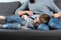 The boy is lying on the couch with an abdominal pain near his mother. The concept of custody, parental care, stomach problems,