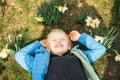 Boy lying on green grass among blooming daffodils on a sunny spring day, smiling with closed eyes Royalty Free Stock Photo
