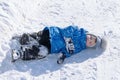 Boy lying on the white snow in clothing. On the street a Sunny day. Winter, cold, frost. A small child fell on to the snow on the Royalty Free Stock Photo