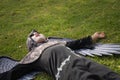 Boy in make up with white face and black eyes, dressed as an angel of death with wings, lying on his back on the grass with a lost