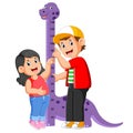 The boy is measuring his sister on the dinosaur measure height