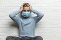 A boy in a medical mask holds his head with his hands. A 9-year-old boy in a blue sweater. Quarantine during the coronavirus