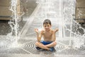 Boy meditating in water fountain find ZEN. Child playing with a city fountain on hot summer day. Happy kids having fun in fountain Royalty Free Stock Photo