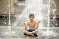 Boy meditating in water fountain find ZEN. Child playing with a city fountain on hot summer day. Happy kids having fun in fountain Royalty Free Stock Photo