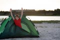 Boy meets dawn in tent on the river bank. Camping holiday in countryside