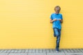 Boy with mobile cell phone standing near yellow wall outdoors Royalty Free Stock Photo