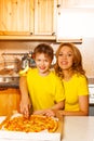 Boy and mother looking forward slicing pizza Royalty Free Stock Photo