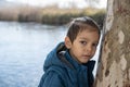 A boy near the tree by the river with expressionless gaze