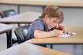 Boy, notebook and writing in school, classroom or studying academic assessment, learning lesson or test at table Royalty Free Stock Photo