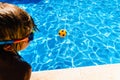 Boy observing a ball moving away from him in a pool in summer, concept of achievable goals in childhood