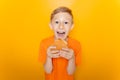 Boy in an orange T-shirt holds a hamburger in front of him and laughs loudly against a yellow background