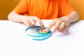 Boy in an orange T shirt sits at a white table and adjusts the twisted thin paper strips with his fingers performs crafts in the