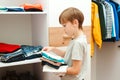 Kid putting stack of clothes on the shelf. Order in the closet. Wardrobe with child`s clothing