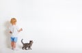 Little boy with paint brush and small cat standing back near white wall Royalty Free Stock Photo