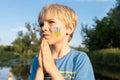 boy with painted trident and a Ukrainian flag on his cheek folded his hands in a prayer-appeal to God