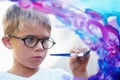 Boy painting on glass, brush and creating artwork with glasses, education and learning. Person, child and kid with art