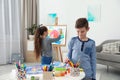 Boy painting at table and girl near easel indoors