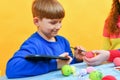 A boy paints Easter eggs with a paintbrush with the help of his older sister