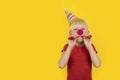 Boy with party hat and red clown nose holding whistle. Portrait on yellow background. Holiday matinee Royalty Free Stock Photo