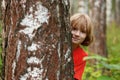 Boy peeking out from behind a tree trunk Royalty Free Stock Photo