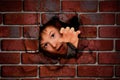 Boy peeking out of a hole in a brick wall