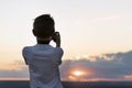 Boy photographs the sunset. Child with camera on setting sun background. Rear view
