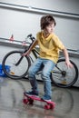Boy with pink penny board, bicycle behind